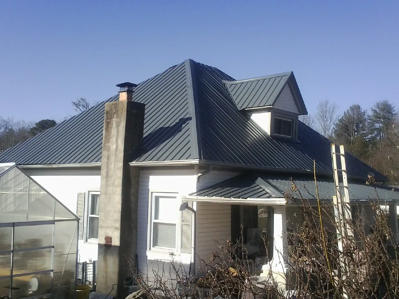 Dark blue standing seam metal roof on a white farmhouse with dormer — Slate & Tile Roof Repair by Roofing Brothers in Rossford
