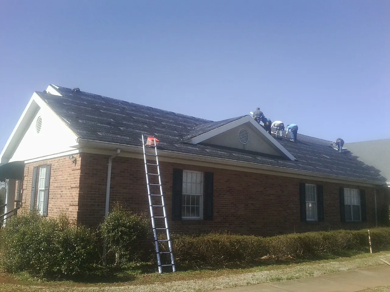 Crew tearing shingles off a brick ranch roof with a ladder set — Emergency Roof Repair work by our crew in Rossford