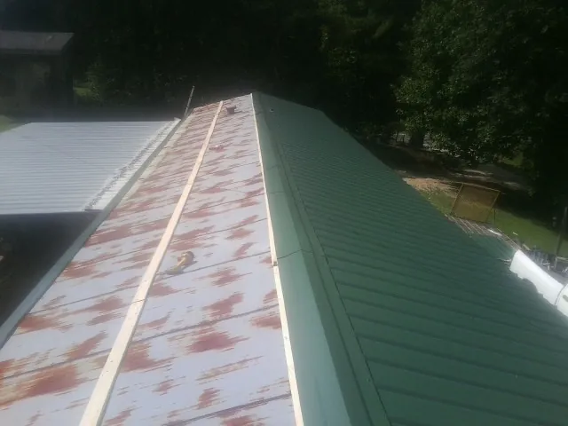 Old rusted panels beside newly installed green metal roofing — Wind Damage Roof Repair by Roofing Brothers in Rossford