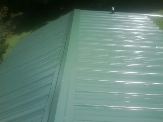 New green metal panels meeting at the ridge of a roof — Flat Roof Repair work by our crew in Rossford