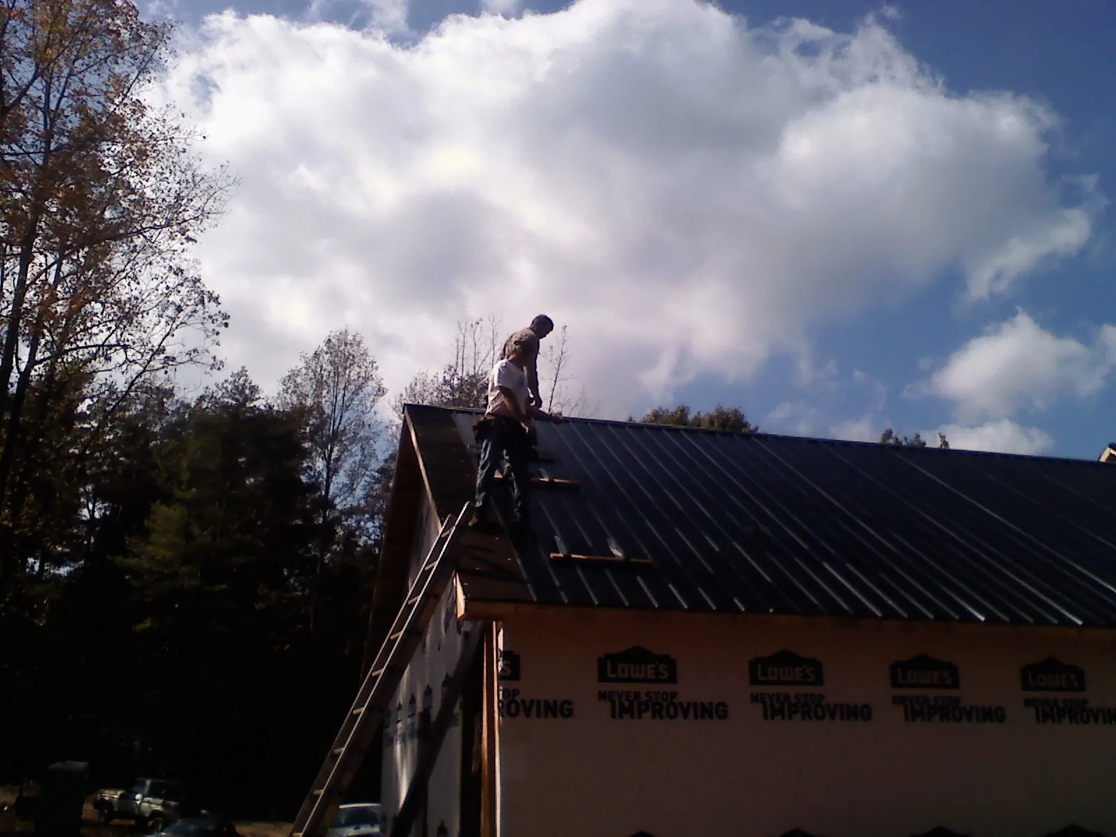Roofer fastening dark metal panels high against a cloudy sky, from a Roof Inspection job in Rossford