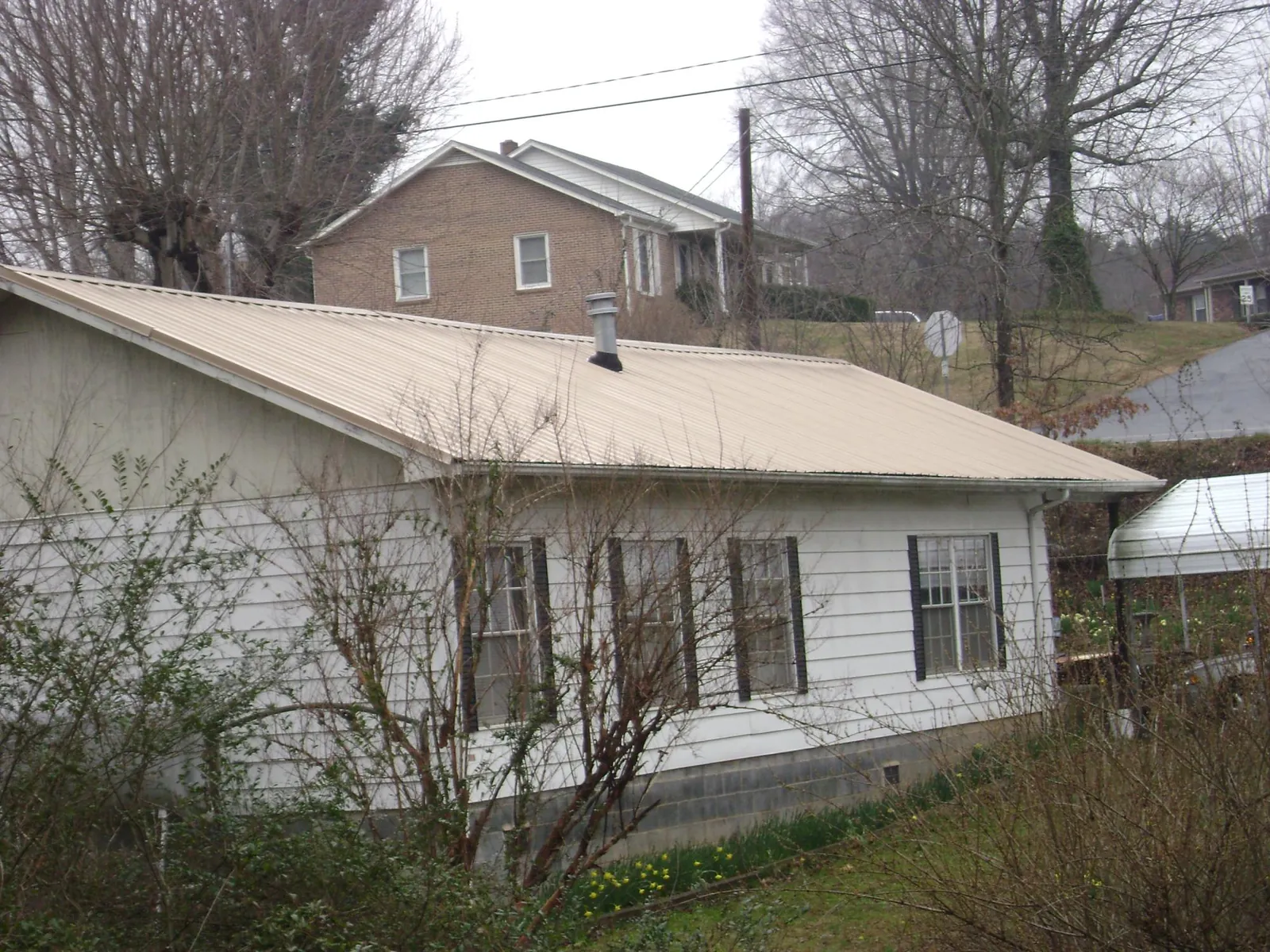 Tan metal roof on a white sided house set into a hillside — Commercial Roofing by Roofing Brothers in Rossford